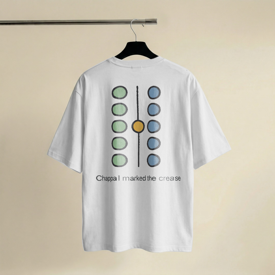 Abstract diagram of two columns of five small circular marks, the left column coloured sage and the right column dusty steel blue, a single honey-gold mark sitting on the dividing centre line between them, with a simple charcoal sans-serif caption underneath about a chappal marking the crease, on a white oversized t-shirt