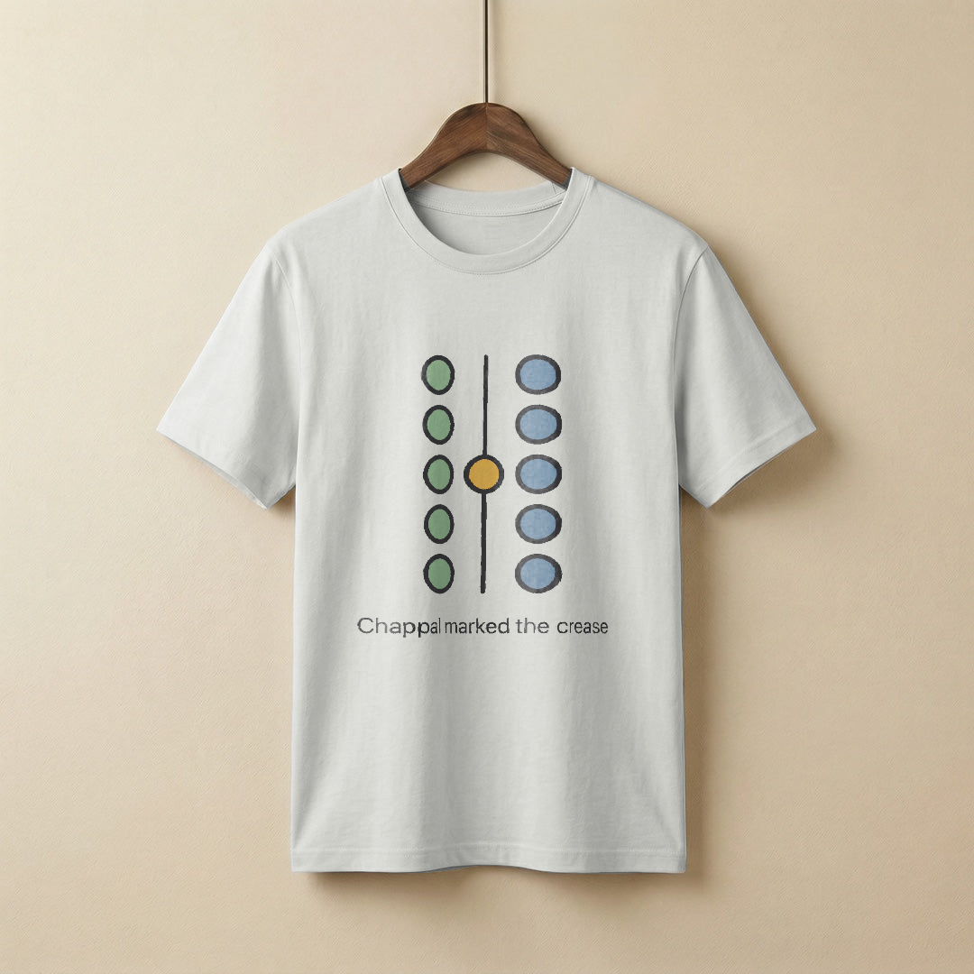 Abstract diagram of two columns of five small circular marks, the left column coloured sage and the right column dusty steel blue, a single honey-gold mark sitting on the dividing centre line between them, with a simple charcoal sans-serif caption underneath about a chappal marking the crease, on a white t-shirt