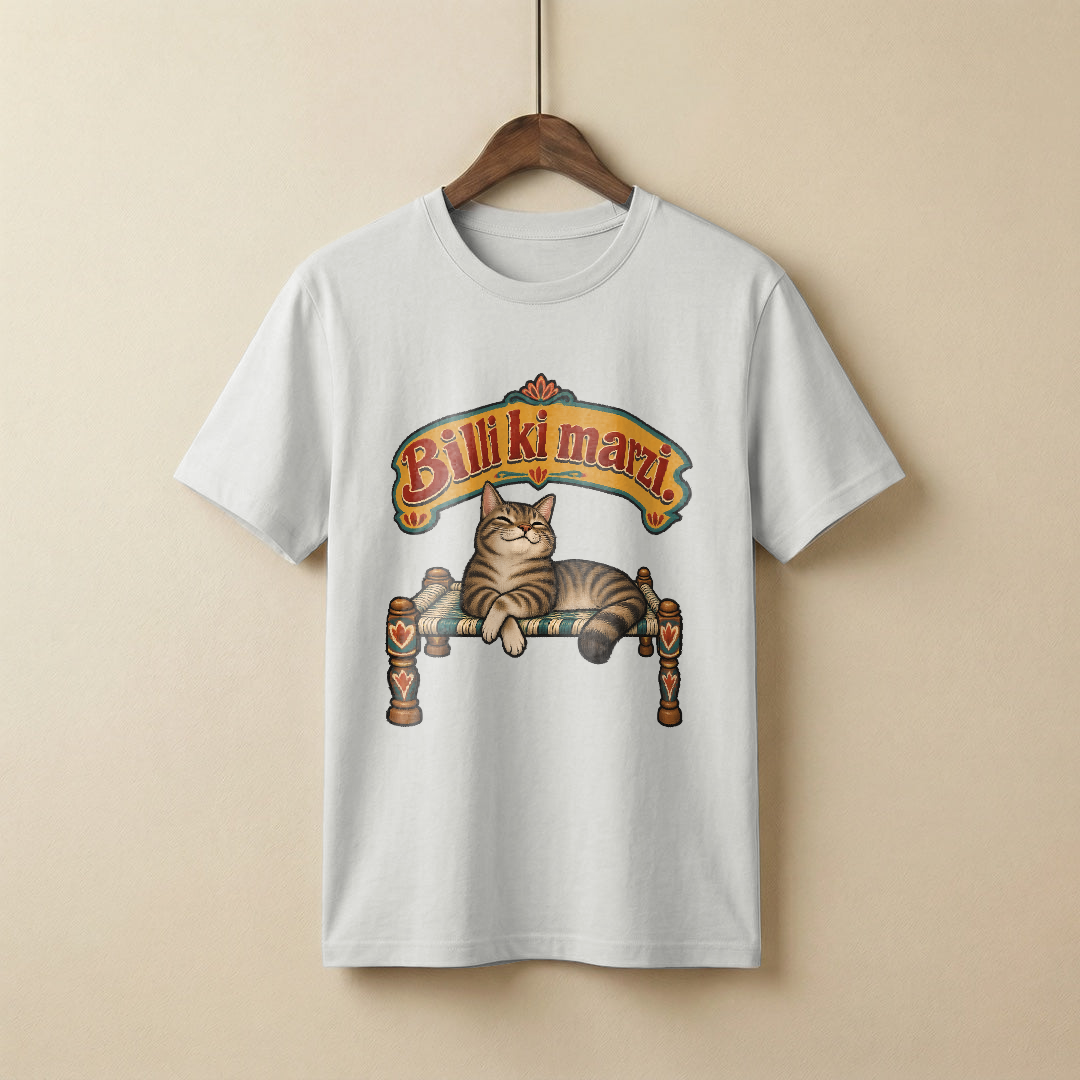 Fat arched signboard lettering reading Billi ki marzi in mustard with red shadowing, above a flat painted tabby cat lounging on a woven charpai with its front paws crossed and eyes half closed, looking very pleased with itself, teal and cream fills with thick black outlines, on a white t-shirt